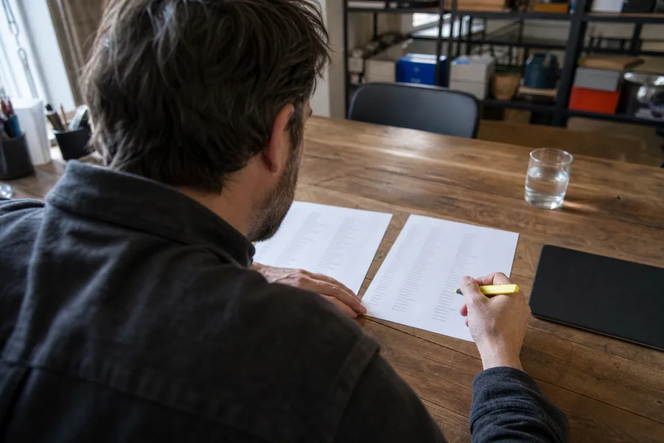 A content lead comparing two printed keyword lists on a meeting table, one hand holding a highlighter